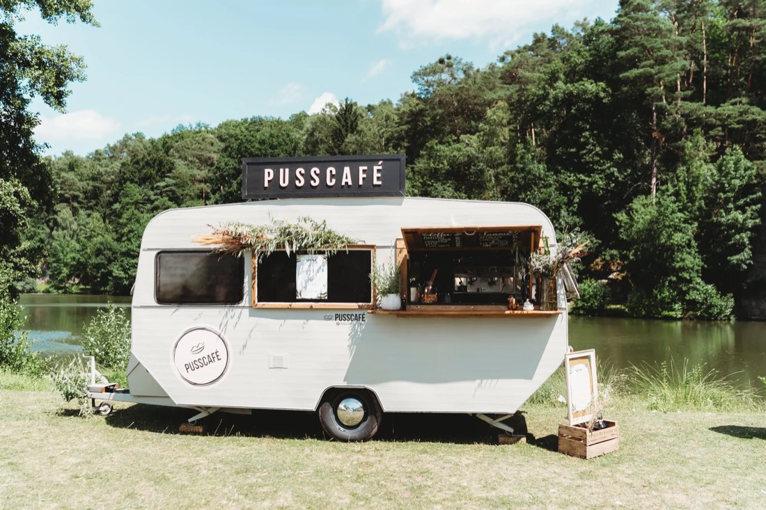 Bílý retro karavan Pusscafé u jezera obklopený lesem
