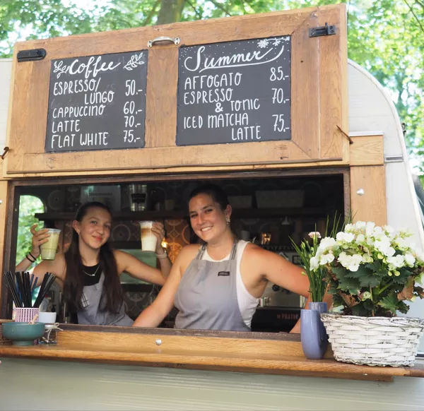 Dvě baristky s úsměvem v okénku karavanu